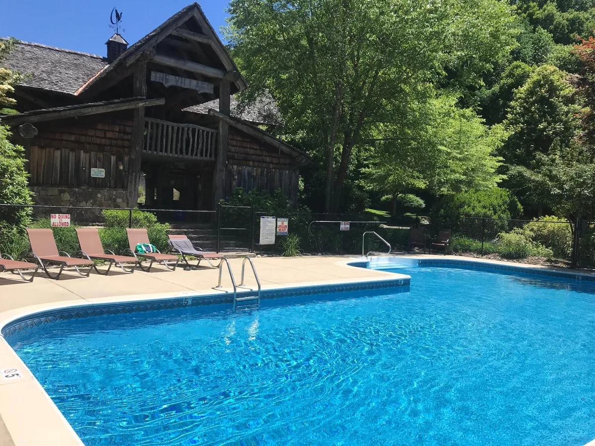 This image features a tranquil resort swimming pool adjacent to a wooden lodge, surrounded by lush greenery. Lounge chairs are set out for sunbathing or relaxing poolside, creating a welcoming atmosphere for both active days and leisurely moments.