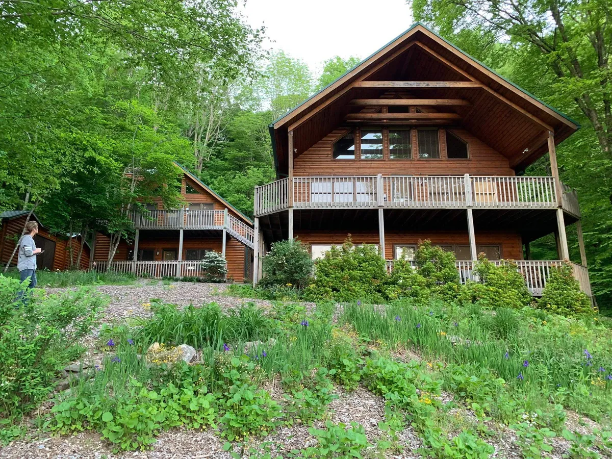 Two wooden houses surrounded by vibrant greenery and flowering plants, with inviting paths leading toward nearby hiking trails. The scene is alive with the feeling of outdoor adventure and exploration, perfect for launching a journey to the Appalachian Trail.