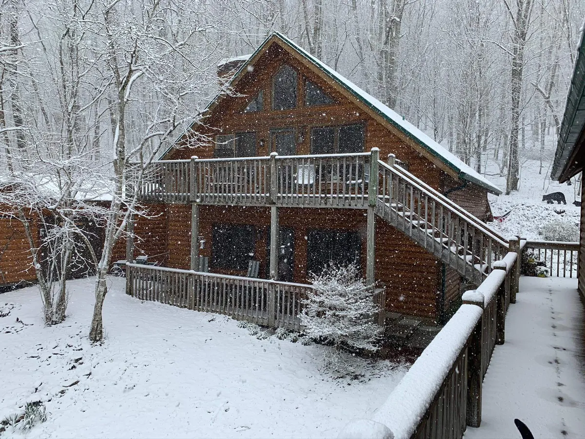 A serene exterior shot of a wooden cabin with a snow-covered deck surrounded by trees, capturing the peacefulness of the gated mountain community. The cozy setting suggests winter retreats, stargazing, and hot cocoa moments.
