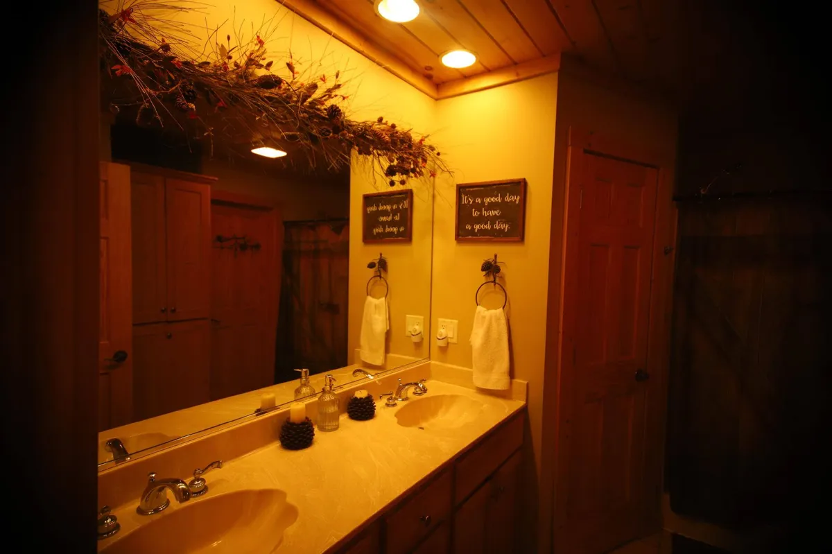 A well-appointed bathroom with dual sinks, a decorative mirror, natural wood cabinetry, and nature-inspired decor. The space is bright, clean, and inviting—the ideal setting for relaxation and personal routines.