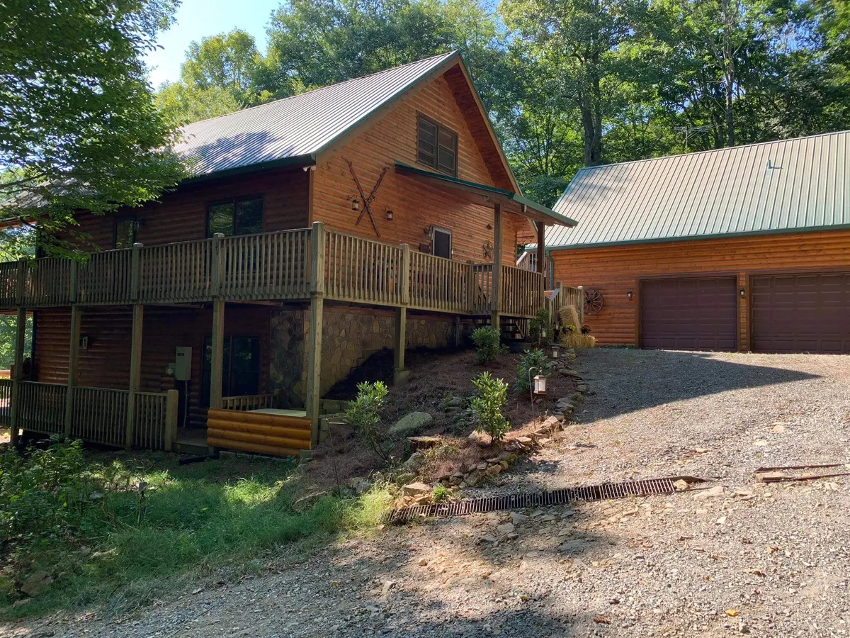A spacious wooden deck set against a stone foundation, surrounded by lush greenery, with hints of a garage nearby. The deck is staged for barbecuing and family gatherings, evoking scenes of outdoor dining and relaxation in nature.